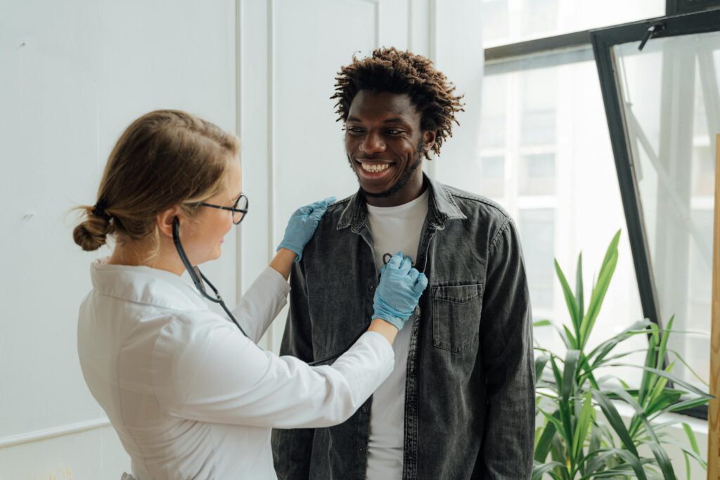 pexels-photo-5215012-5215012 Doctor with stethoscope examining a smiling patient indoors, promoting health and care.