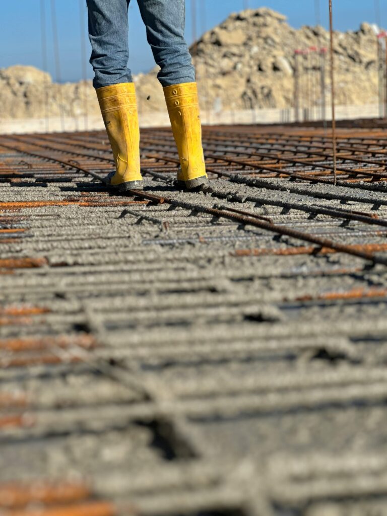 Close-up of a worker standing on a concrete slab with rebar, wearing yellow boots.